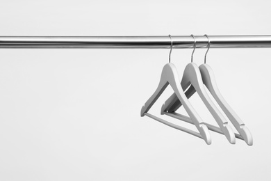 Empty clothes hangers on metal rail against light background. Space for text