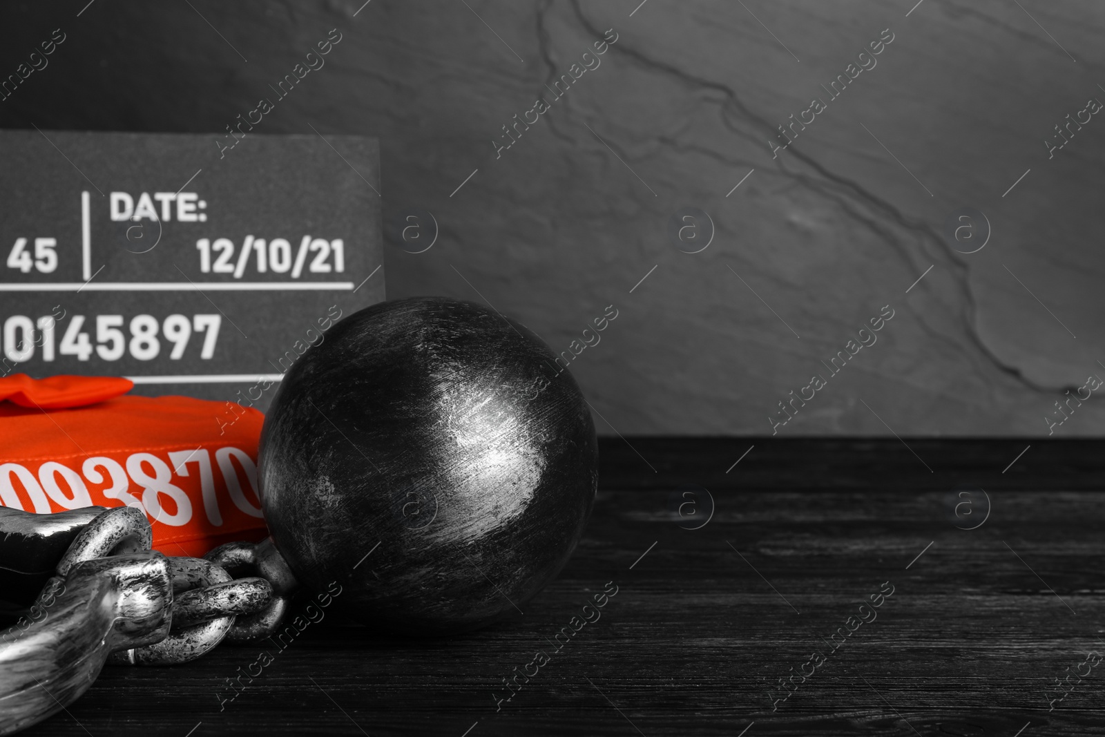 Photo of Metal ball with chain, prison uniform and mugshot letter board on black wooden table, space for text