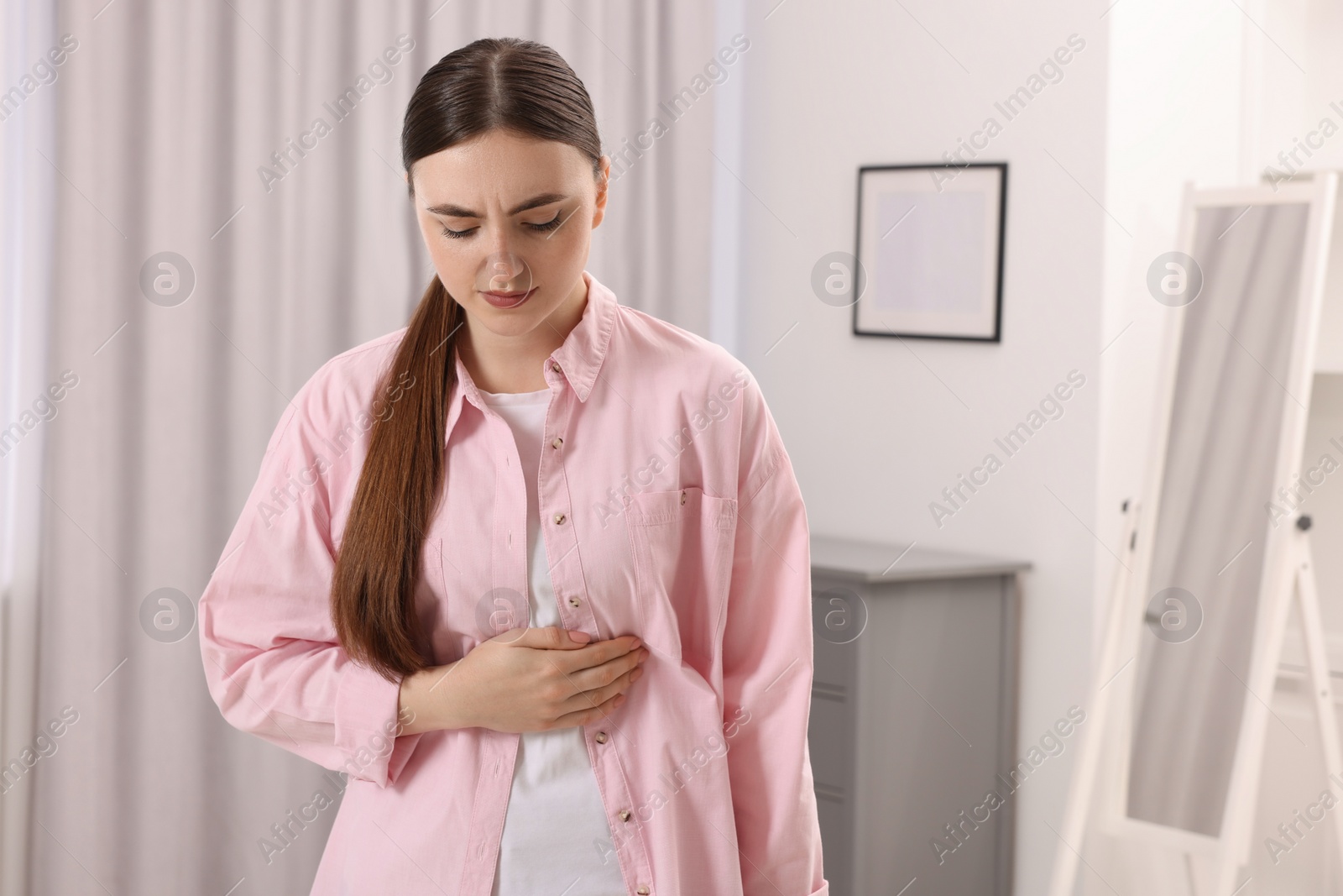 Photo of Young woman suffering from stomach pain at home. Space for text