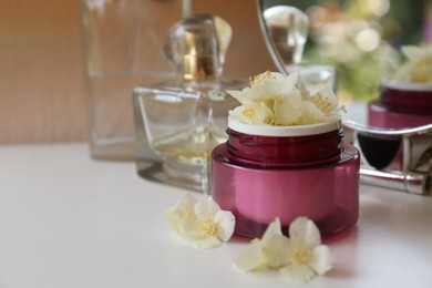 Photo of Jar of cream with beautiful jasmine flowers, perfume and mirror on white table, closeup. Space for text