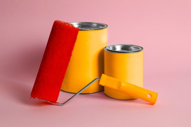 Cans of orange paint and roller on pink background
