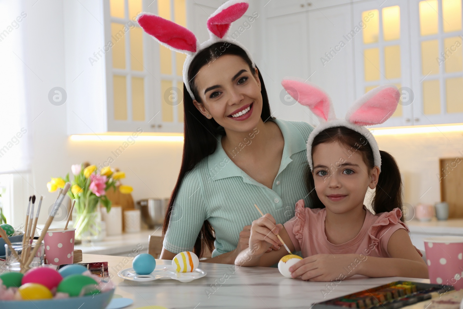 Photo of Happy mother with her cute daughter painting Easter eggs at table in kitchen