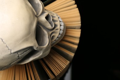 Photo of Human skull and old book on black background, top view. Space for text
