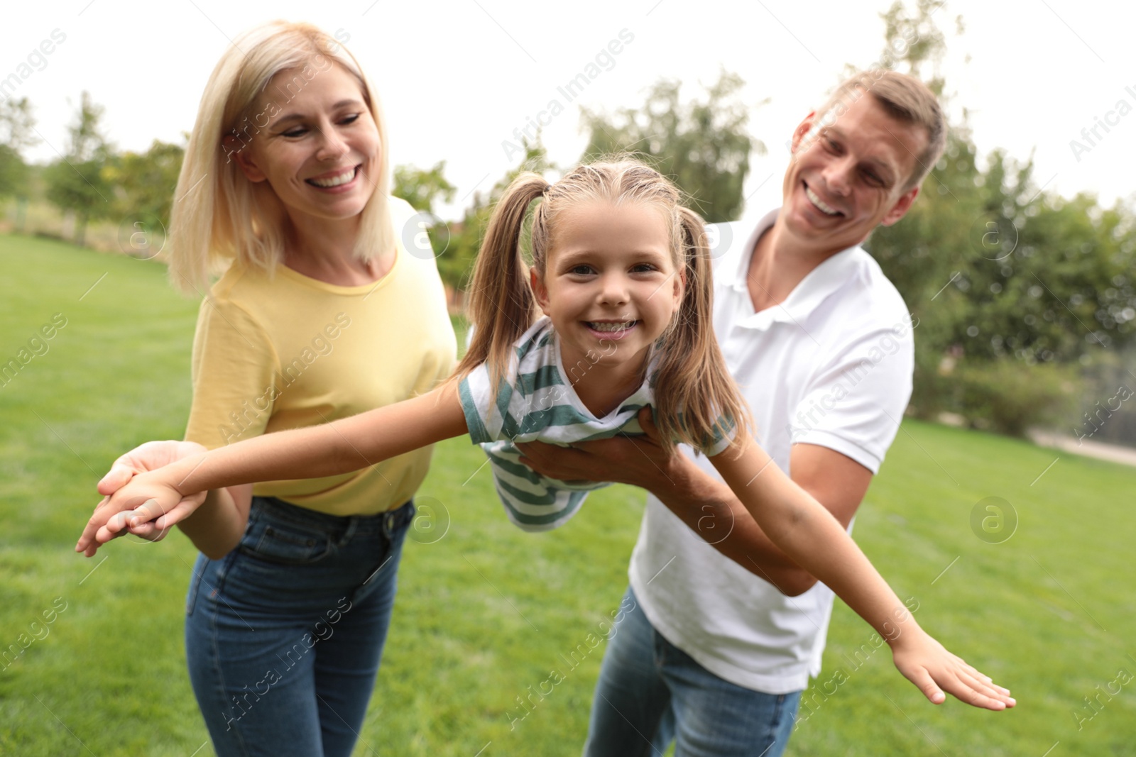 Photo of Cute little girl having fun with her parents in park on summer day