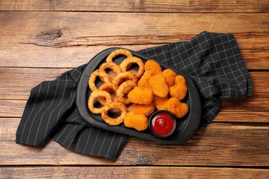 Tasty ketchup, onion rings and chicken nuggets on wooden table, top view