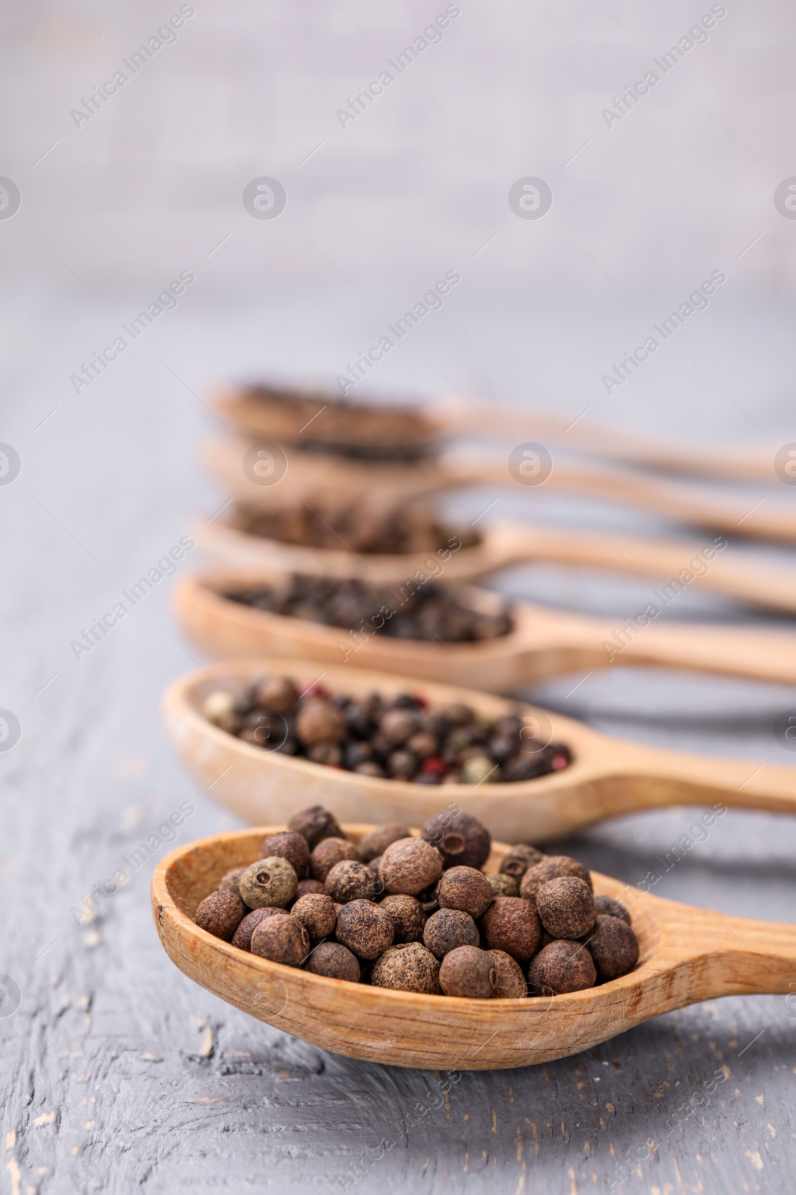 Photo of Spoons with peppercorns on grey wooden table, closeup