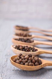 Photo of Spoons with peppercorns on grey wooden table, closeup