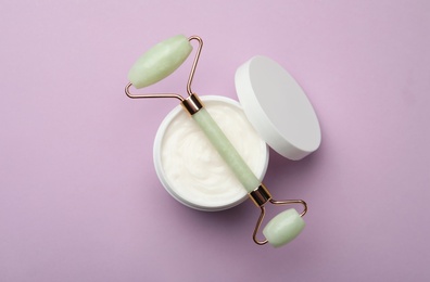 Natural face roller and cosmetic product on pink background, top view