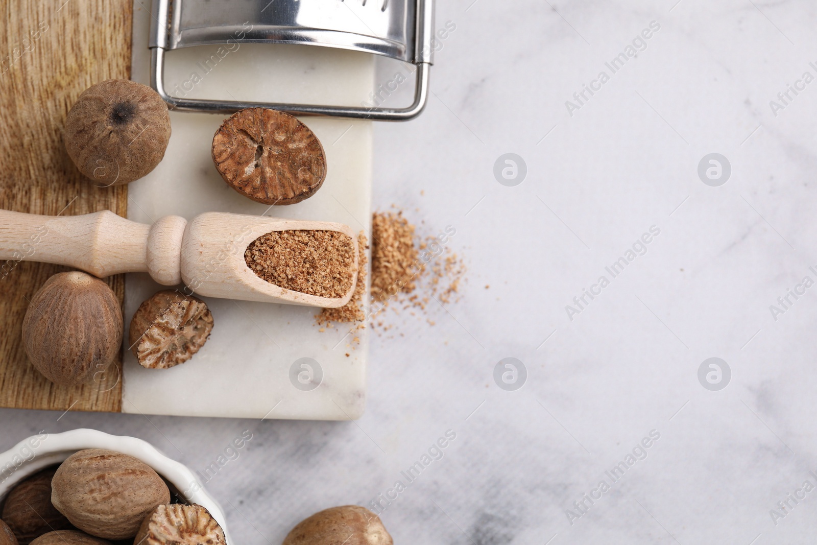 Photo of Scoop with grated nutmeg, seeds and grater on white marble table, flat lay. Space for text