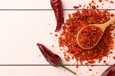 Photo of Chili pepper flakes and pods on white wooden table, flat lay. Space for text