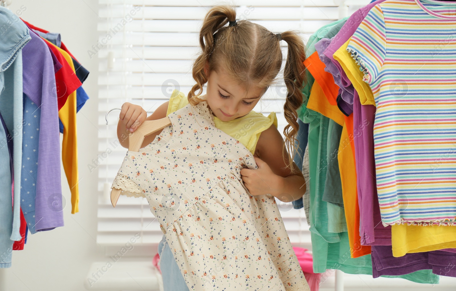Photo of Little girl choosing clothes on racks indoors
