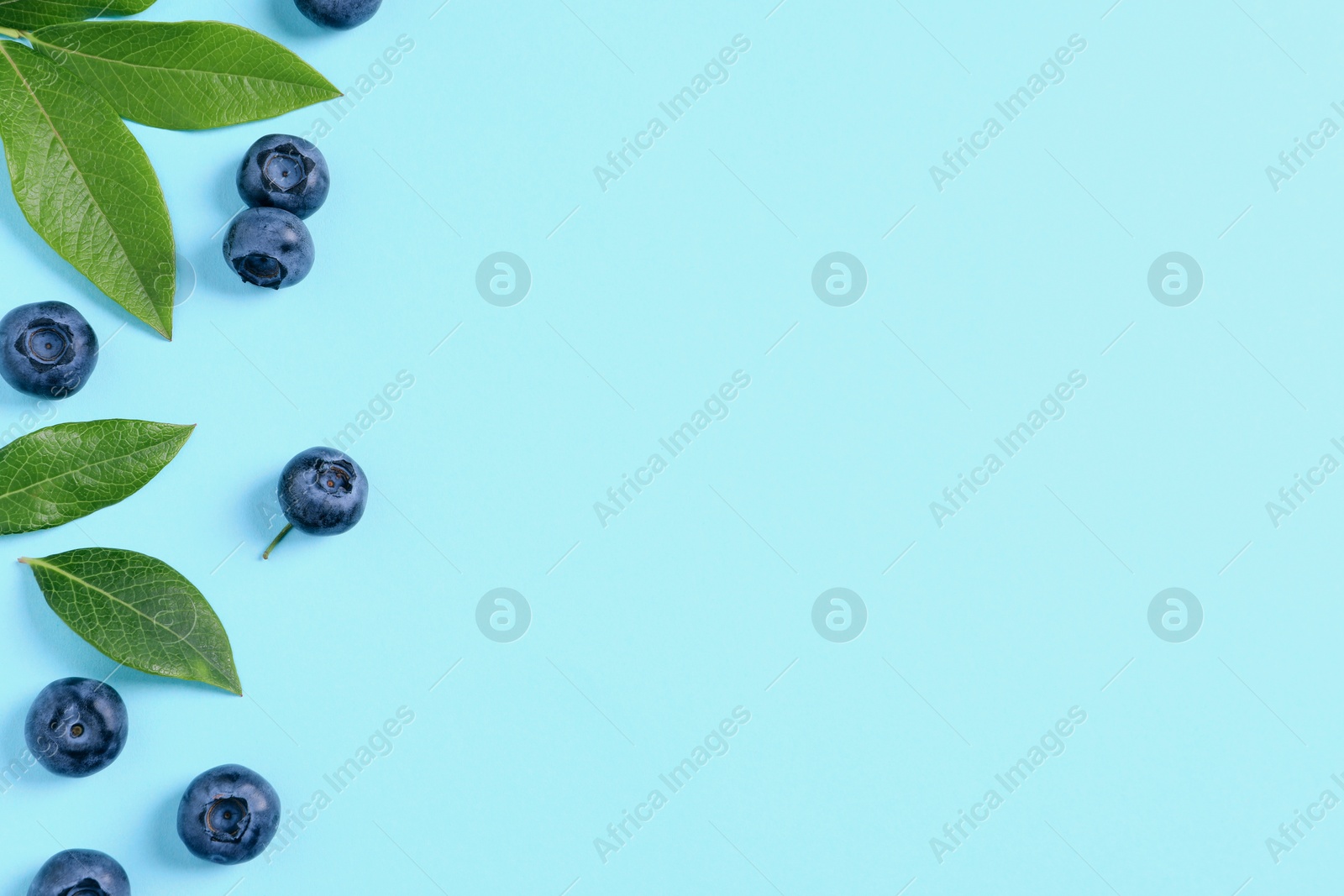 Photo of Tasty fresh blueberries with green leaves on light blue background, flat lay. Space for text