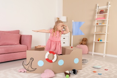 Photo of Cute little girl playing with cardboard ship at home