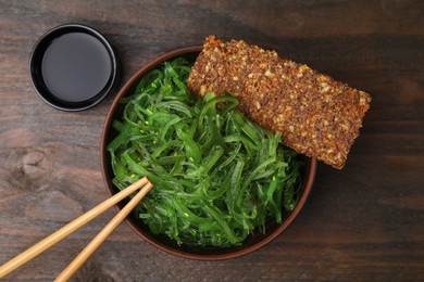 Photo of Tasty seaweed salad in bowl served on wooden table, flat lay