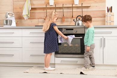 Cute children baking cookies in oven at home