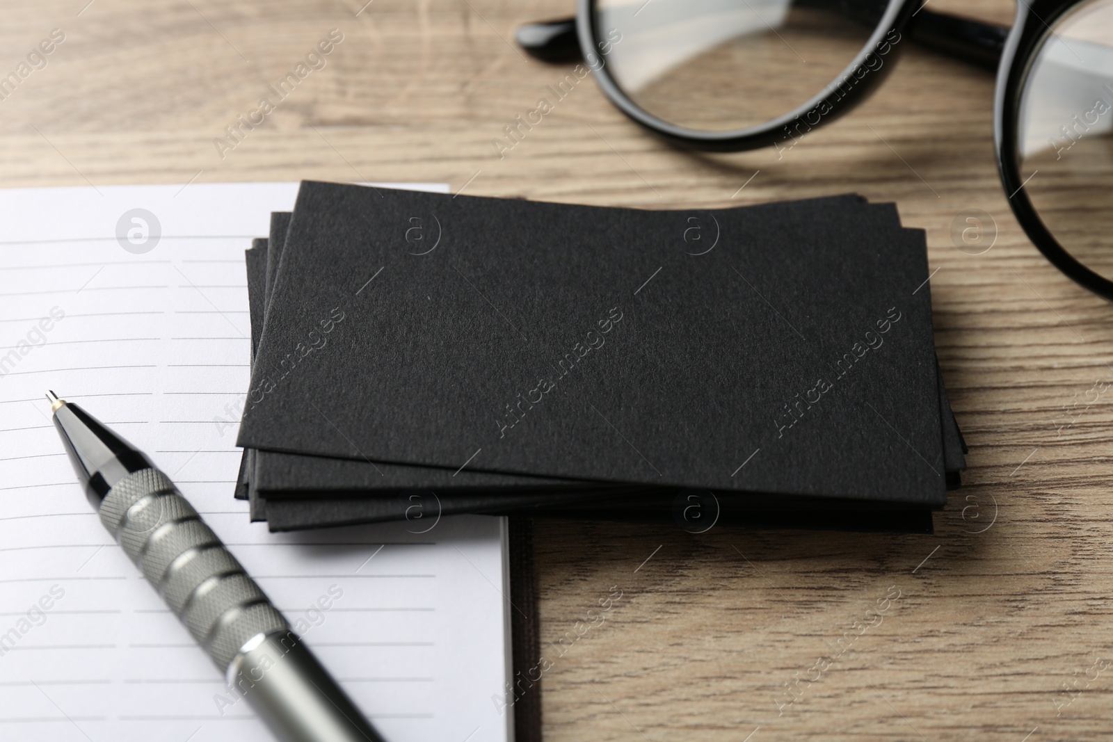 Photo of Blank black business cards, notebook, glasses and pen on wooden table, closeup. Mockup for design