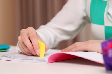Photo of Girl erasing mistake in her notebook at white desk indoors, closeup