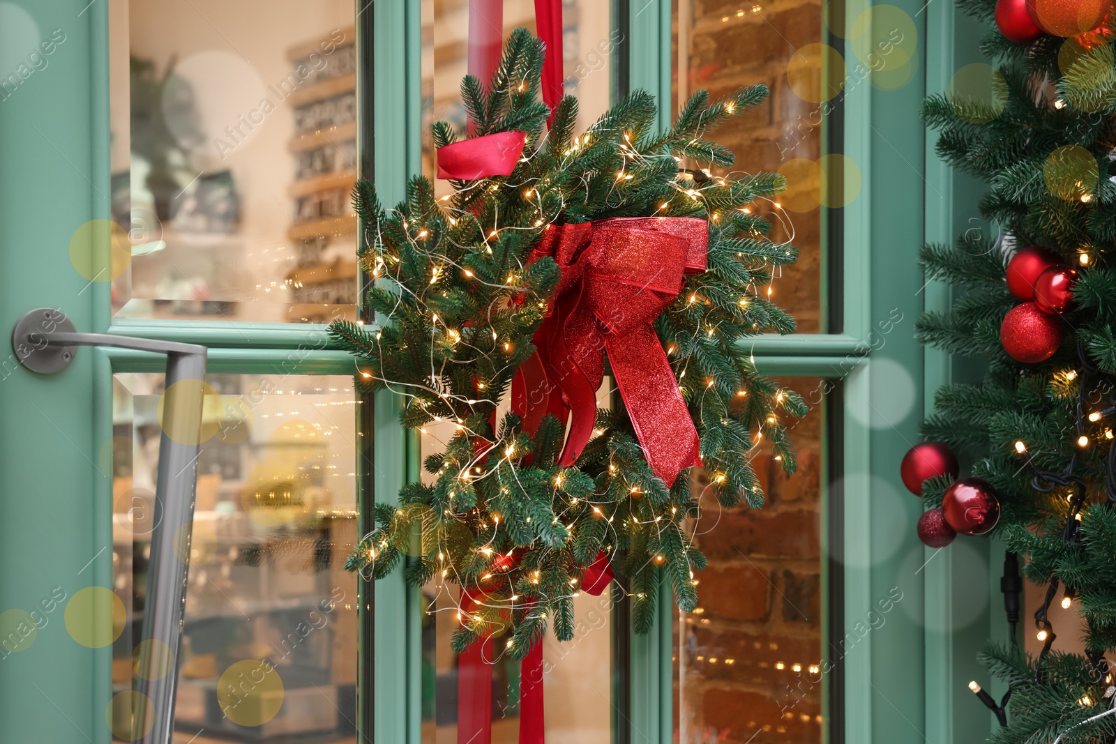 Photo of Beautiful Christmas wreath with ribbon and festive lights hanging on door