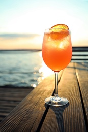 Photo of Glass of fresh summer cocktail on wooden table outdoors at sunset