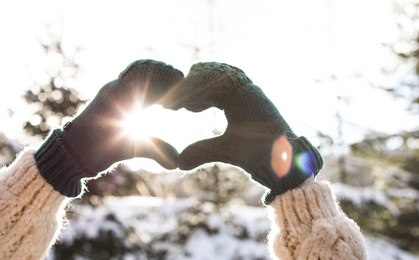 Photo of Young woman making heart with hands outdoors, closeup. Winter vacation