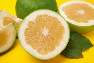 Whole and cut sweetie fruits with green leaves on yellow background, closeup