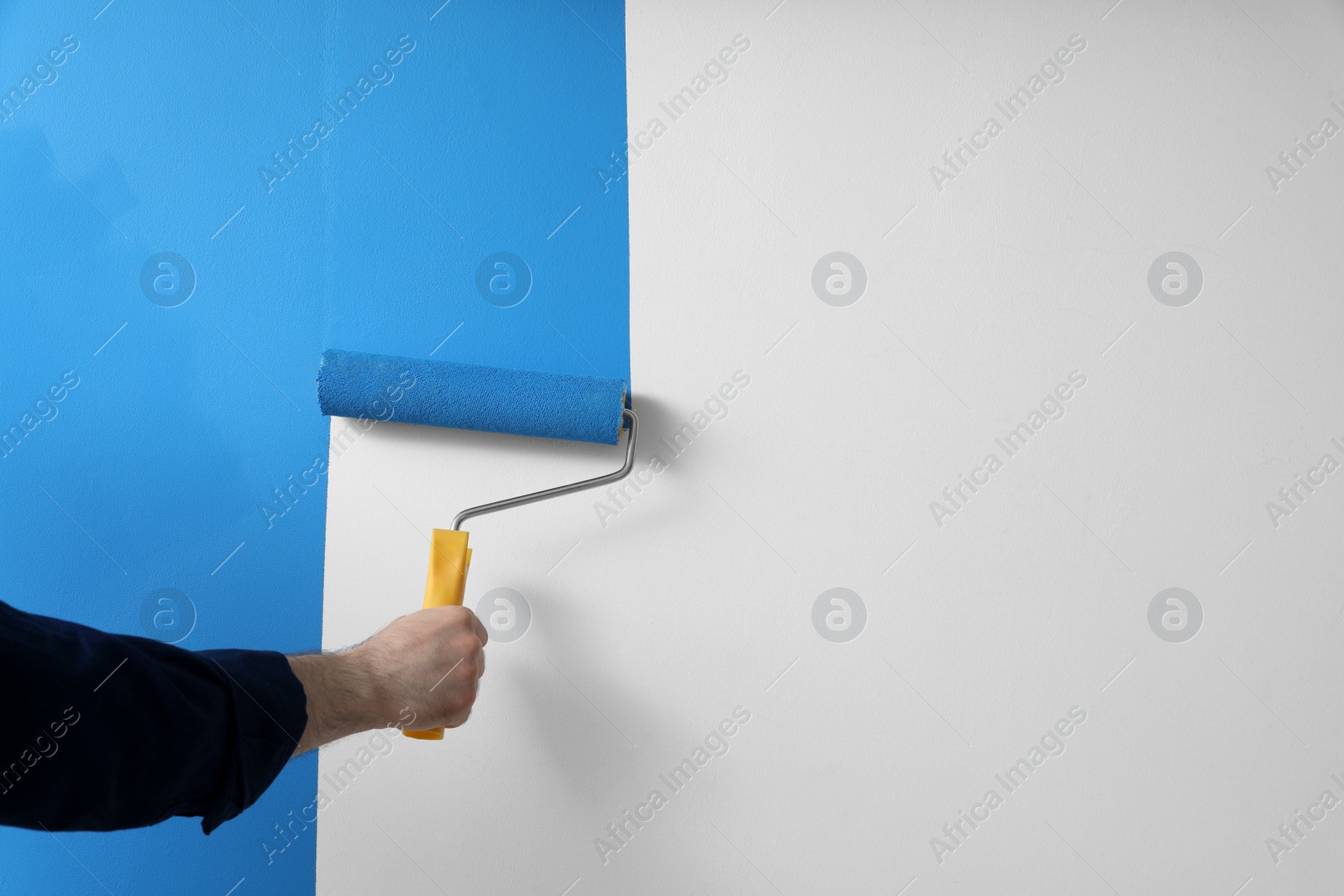 Photo of Man applying light blue paint with roller brush on white wall, closeup