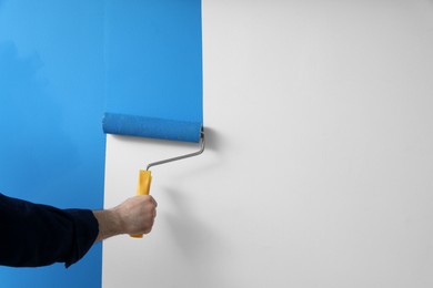 Man applying light blue paint with roller brush on white wall, closeup