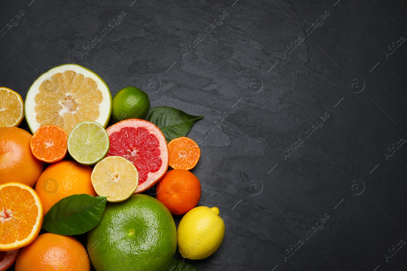 Photo of Different ripe citrus fruits with green leaves on black table, flat lay. Space for text