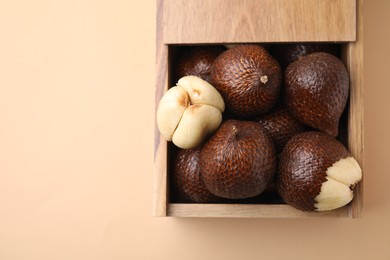 Wooden crate with fresh salak fruits on beige background, top view. Space for text