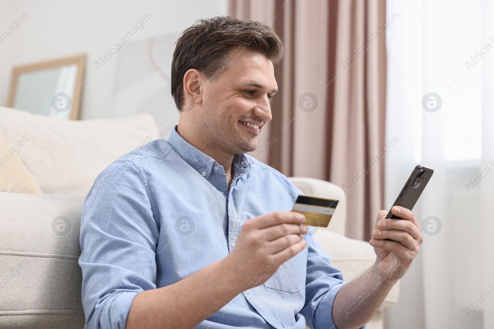 Photo of Happy man with credit card using smartphone for shopping online at home