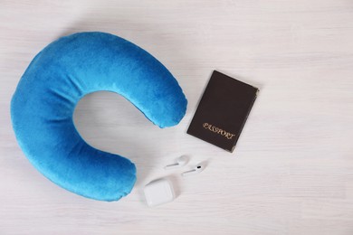 Photo of Light blue travel pillow, passport and earphones on white wooden background, flat lay