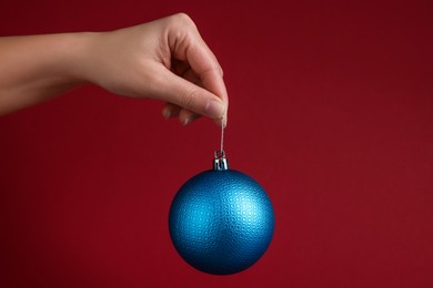 Photo of Woman holding blue Christmas ball on red background, closeup