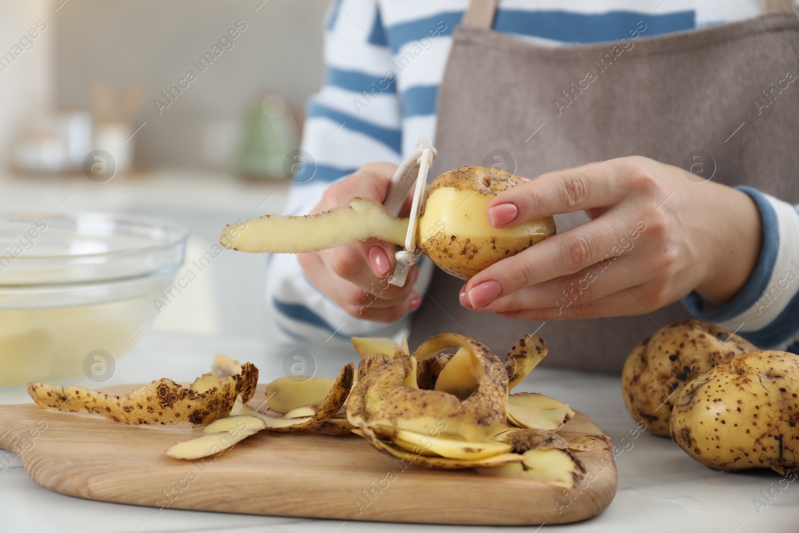 Photo of Woman peeling fresh potato at white marble table indoors, closeup