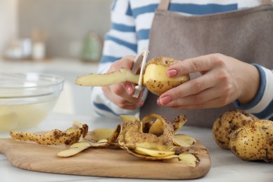 Photo of Woman peeling fresh potato at white marble table indoors, closeup