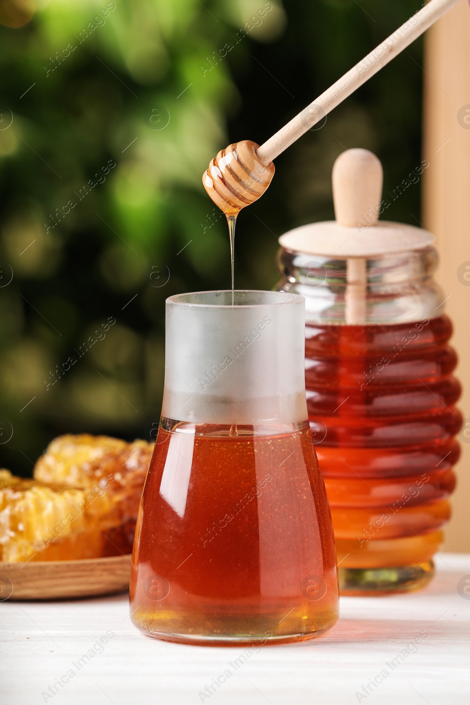 Photo of Dripping tasty honey from dipper into jar on white wooden table