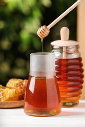 Photo of Dripping tasty honey from dipper into jar on white wooden table