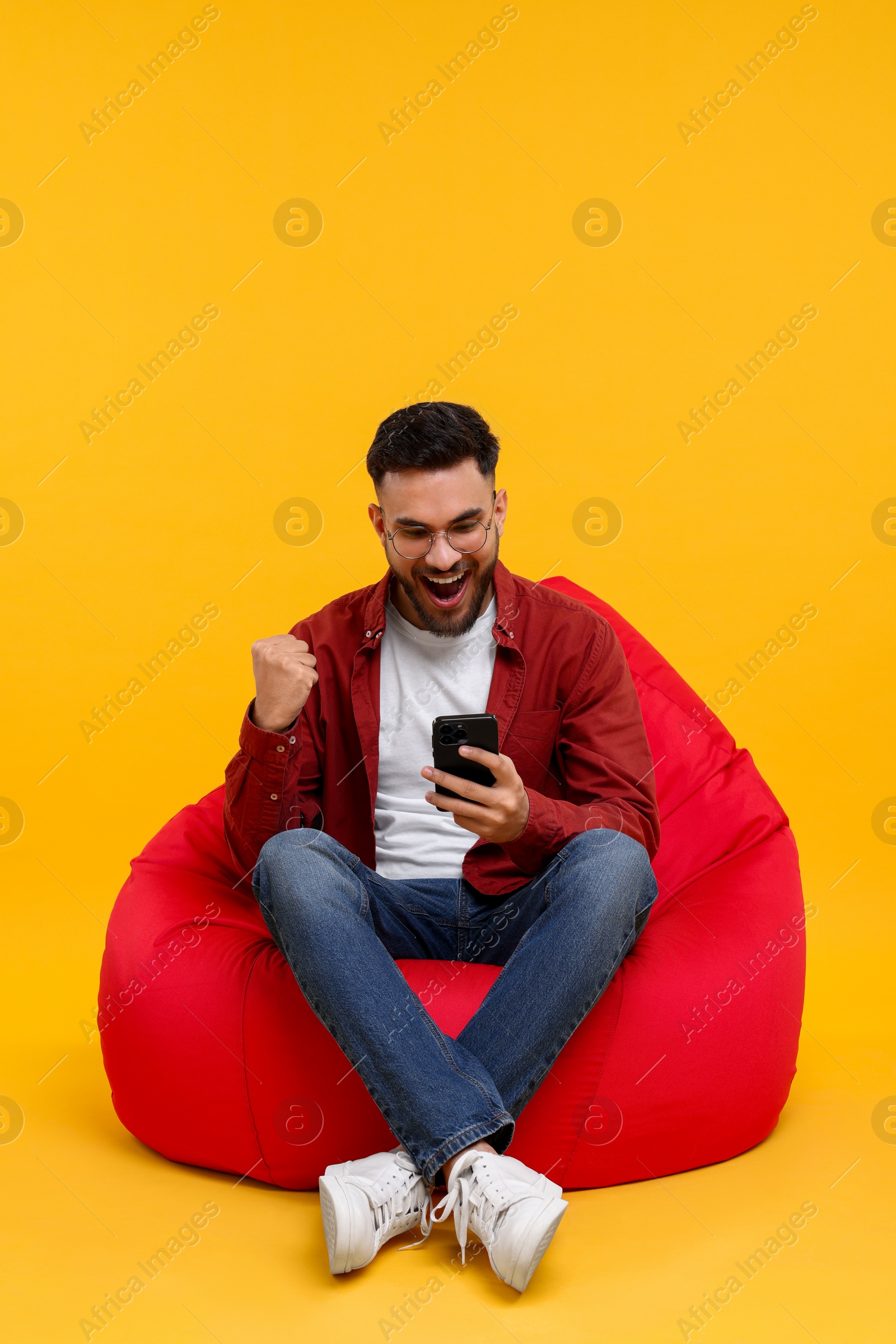 Photo of Happy young man using smartphone on bean bag chair against yellow background