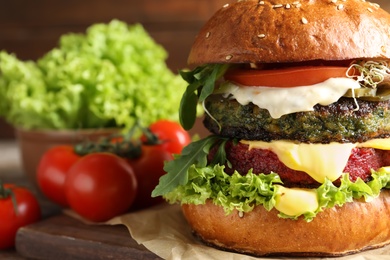 Photo of Vegan burger with beet and falafel patties on table against blurred background, closeup