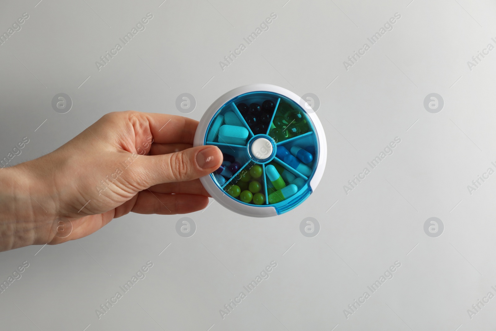 Photo of Woman holding plastic box with different pills on light grey background, closeup