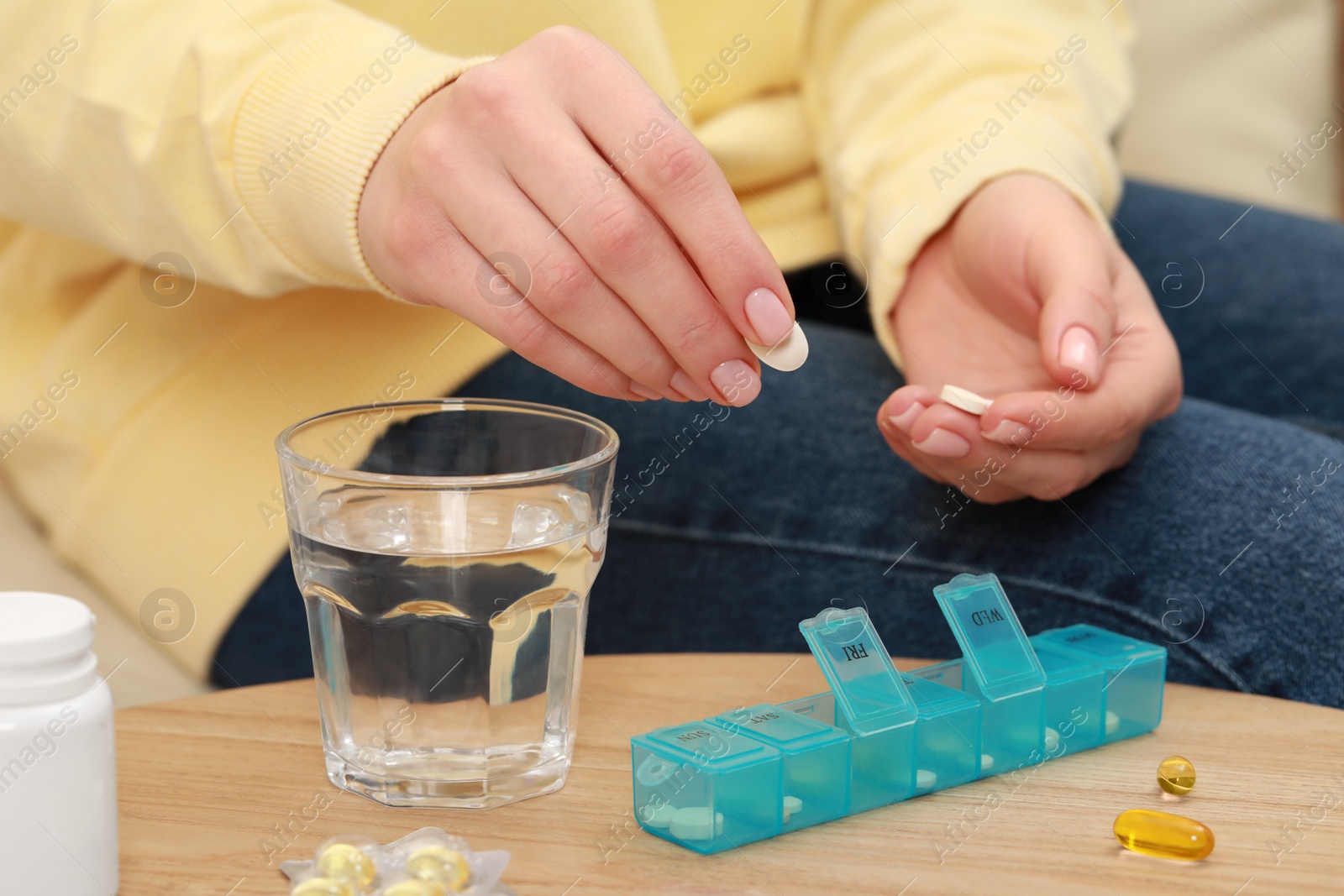 Photo of Woman taking pill from plastic box at wooden table, closeup