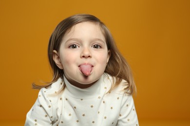 Photo of Funny little girl showing her tongue on orange background