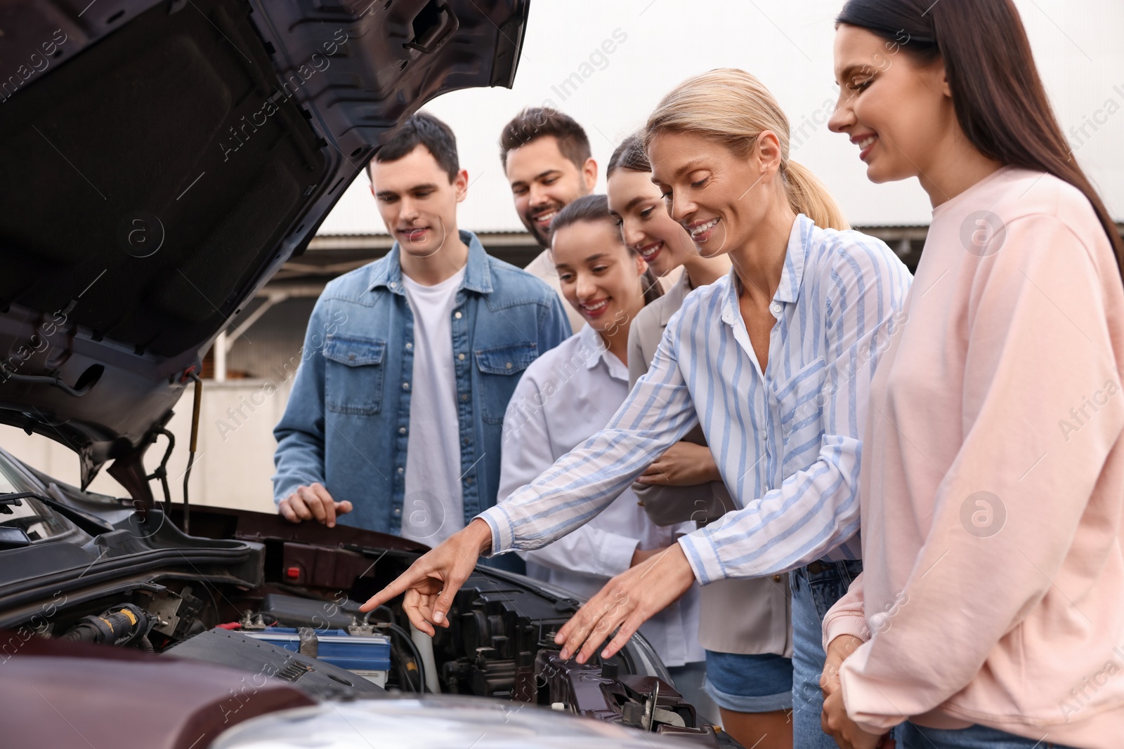 Photo of Driving school. Teacher explaining car engine to group outdoors