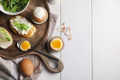 Breakfast with soft boiled eggs served on white wooden table, flat lay. Space for text