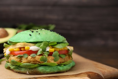 Photo of Tasty green vegan burger with vegetables, patty and microgreens on wooden board, closeup. Space for text