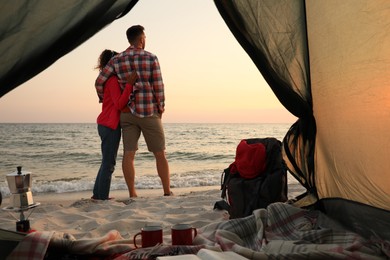 Couple near sea at sunset, view from camping tent