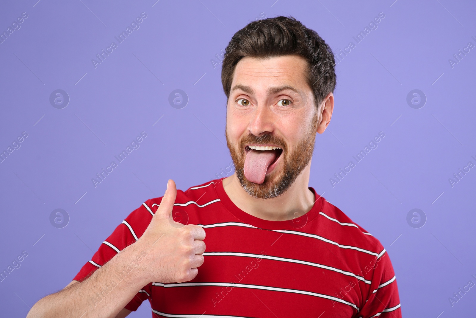 Photo of Man showing his tongue and thumbs up on violet background