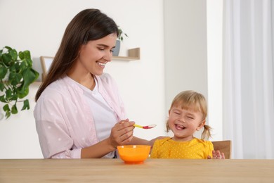 Mother feeding her cute little child with yogurt at wooden table indoors