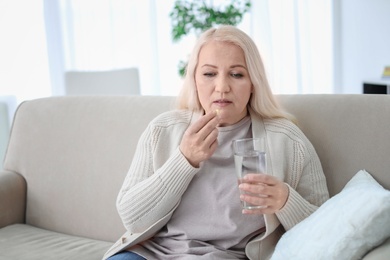 Photo of Mature woman taking pill against headaches on sofa at home