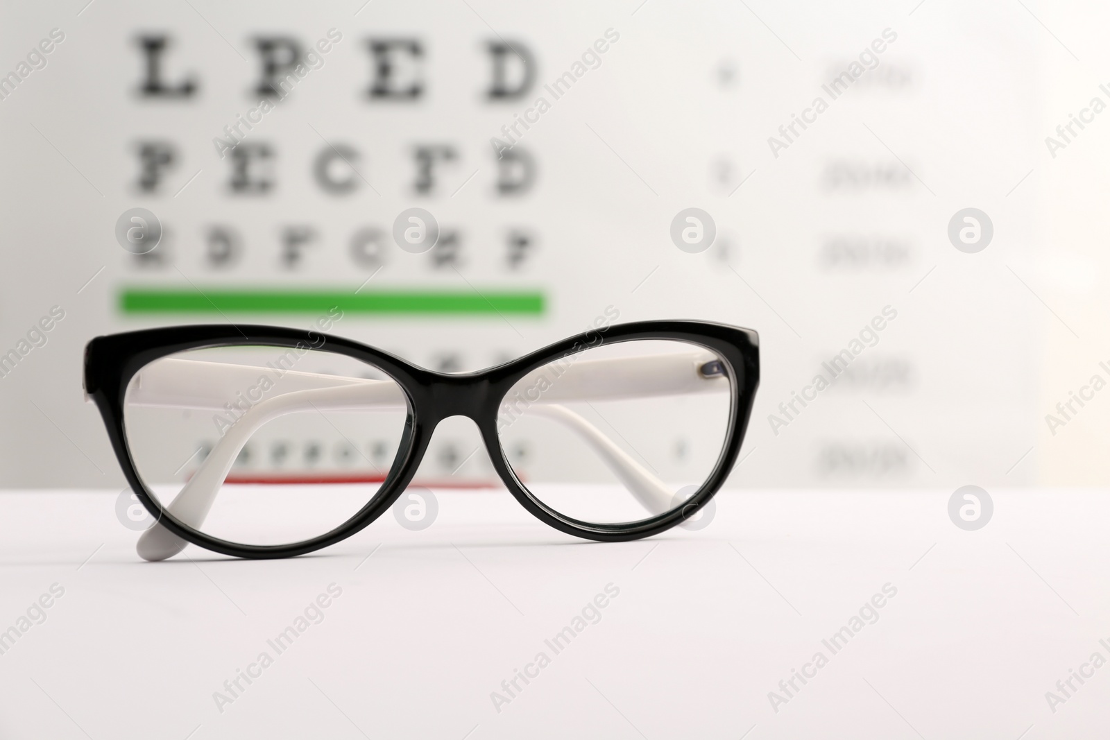 Glasses with corrective lenses on table against eye chart Photo of Glasses with corrective lenses on table against eye chart