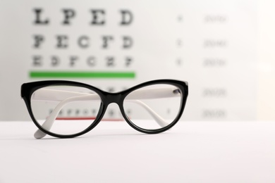 Photo of Glasses with corrective lenses on table against eye chart